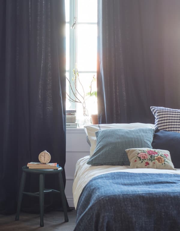 Chambre décorée avec des textiles dans des teintes de bleu et de blanc et des rideaux tombant du plafond jusqu’au sol.