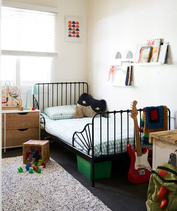 Chambre d'enfant avec des murs blancs, un cadre de lit noir et des livres sur des tablettes pour photos.