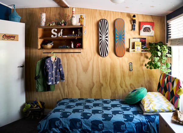Chambre d'enfant avec étagères et planches à roulettes sur un mur en bois et linge de lit à motifs bleus.