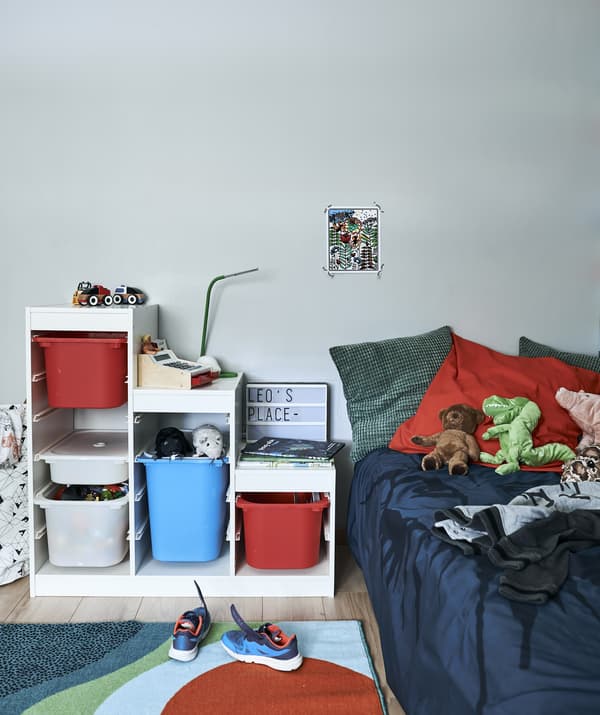Chambre d'enfant avec meuble de rangement, tapis et linge de lit coloré, avec coussins et jouets.