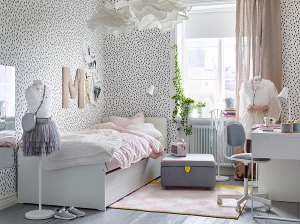 Chambre d'enfant avec murs blancs constellés de taches noires et lit blanc avec linge de lit rose pâle.