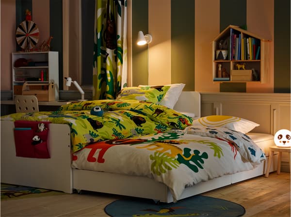 Chambre d'enfant prête pour la nuit, avec literie à motifs animaux et cadre de lit blanc dont le compartiment de rangement est sorti.