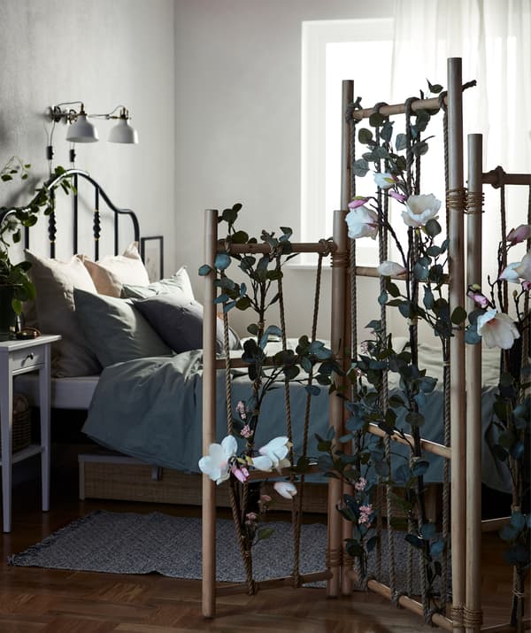 Chambres à coucher dont le lit est séparé du reste de la pièce par un paravent TÄNKVÄRD orné de verdure artificielle.