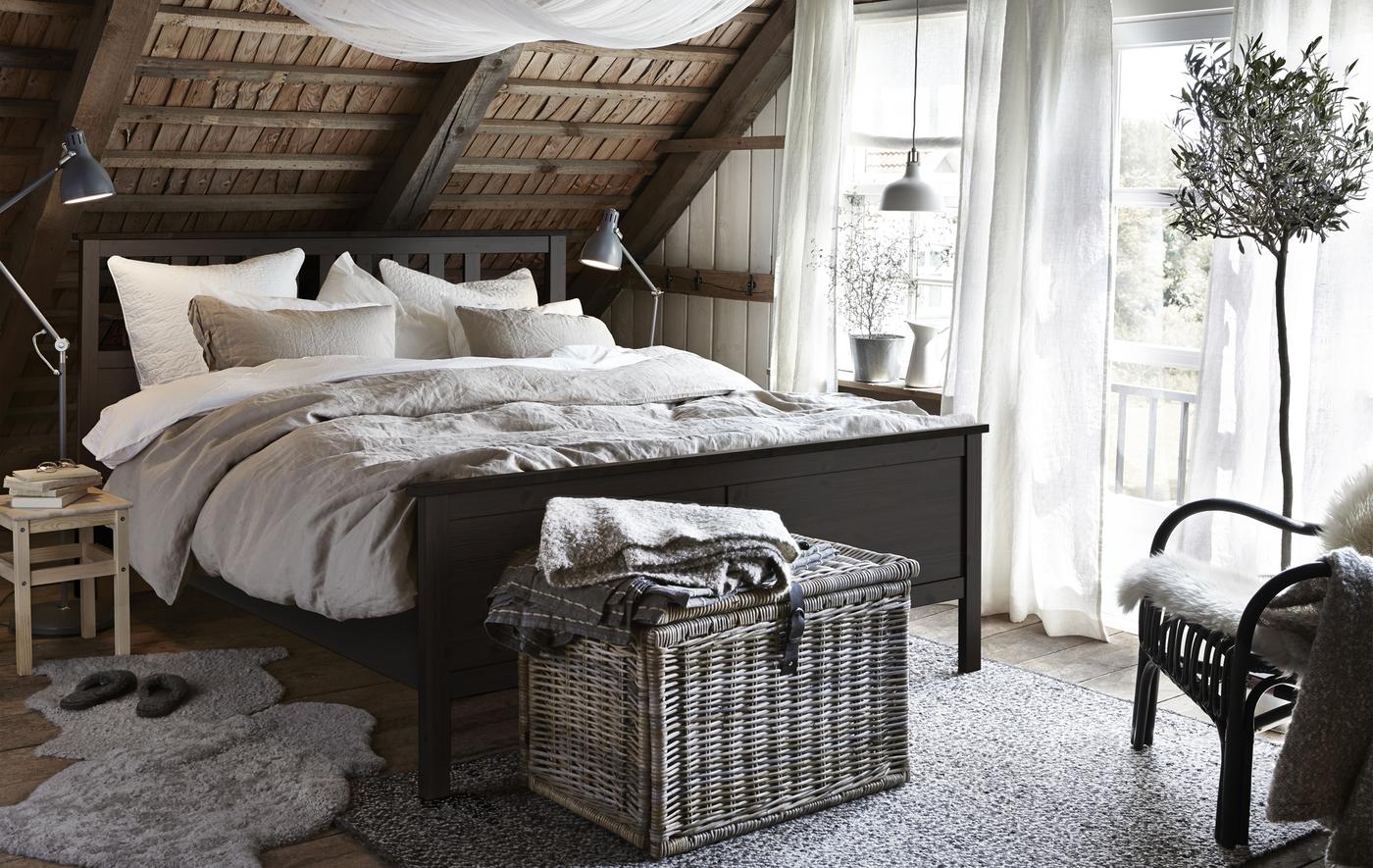 Chambres à coucher rustique avec cadre de lit HEMNES noir-brun, panier en wicker, peaux de mouton posées sur le sol et plafond en sous-pente lambrissé.