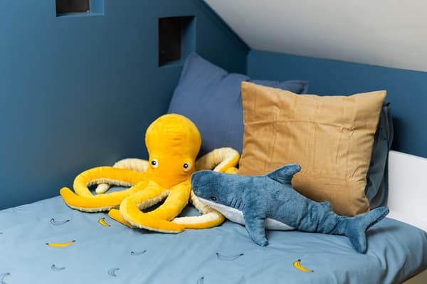 Children’s room with a bed, cushions, and neatly stacked toy storage boxes; a yellow octopus soft toy on the bed.