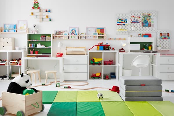 Children’s room with toys across the floor, desks along the side, and drawings on pegboards and FLISAT ledges up the walls.