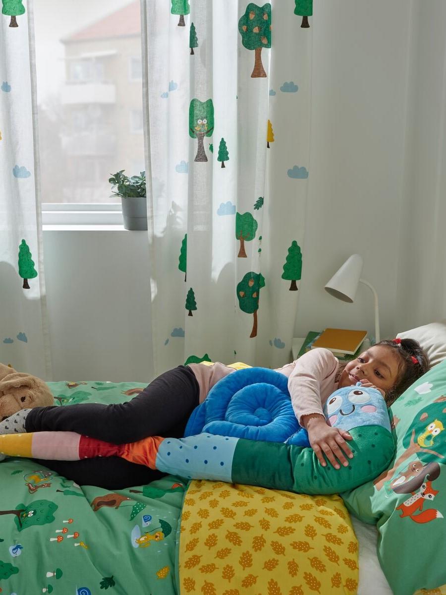 Children’s textiles
Two children resting on a bed with bright, playful printed blankets and a hanging forest-themed mobile.