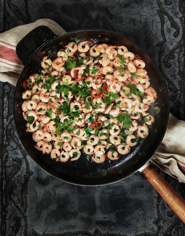 Chilli-tossed shrimps with garlic garnished with parsley, served in a cast iron frying pan, seen from above.