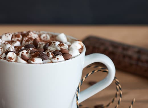 Chocolat chaud garni de miniguimauves et de pépites de chocolat présenté dans une chope blanche.