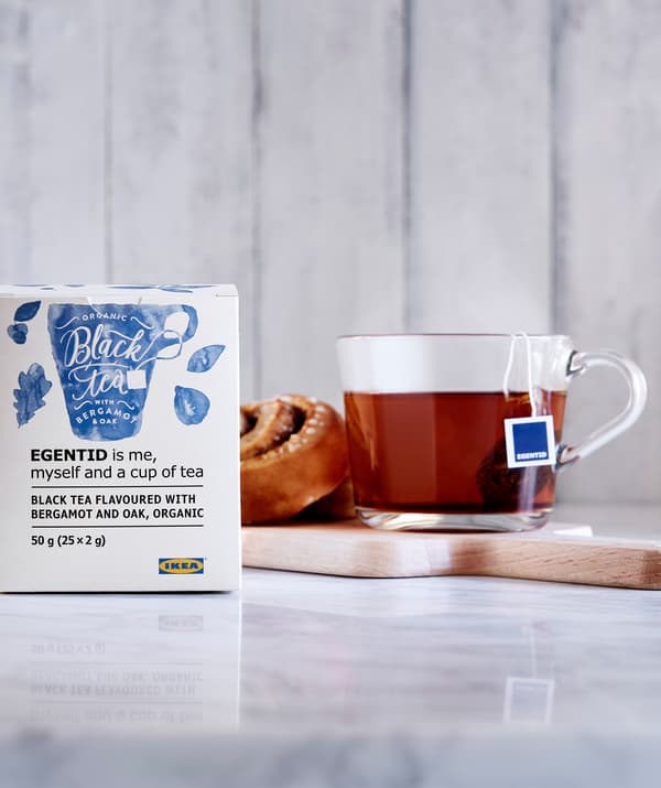 Cinnamon roll and tea in glass cup on small tray, in turn placed on a section of marble worktop; packet of tea on the side.