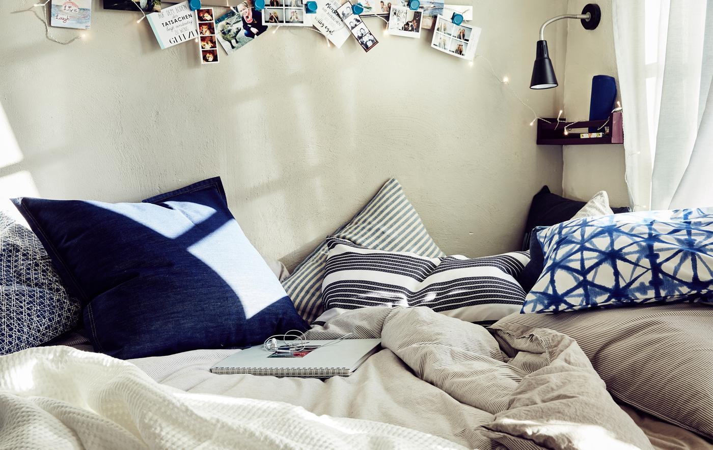 Close-up of a bed with neutral bedding and blue patterned cushions.