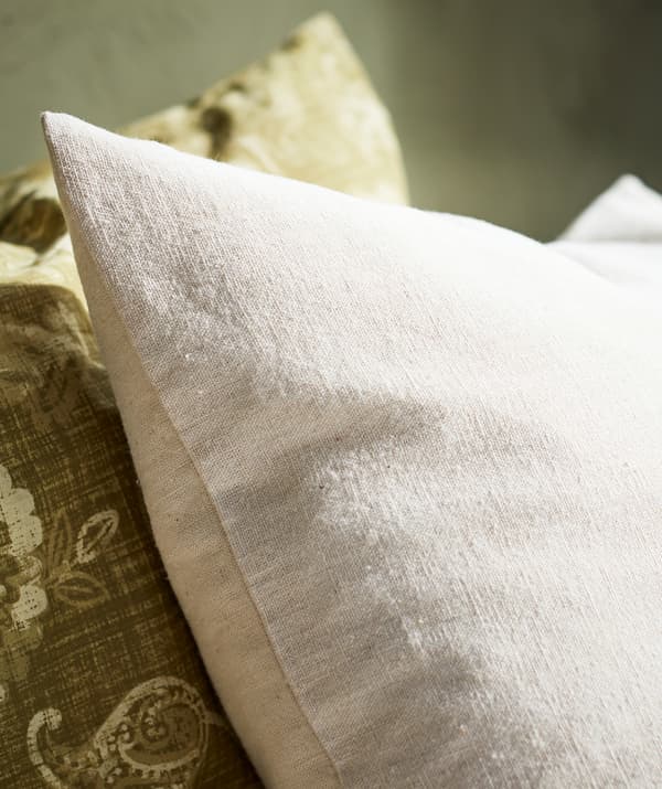 Close-up of a beige pillow in natural cotton material shown next to a green paisley patterned pillow.