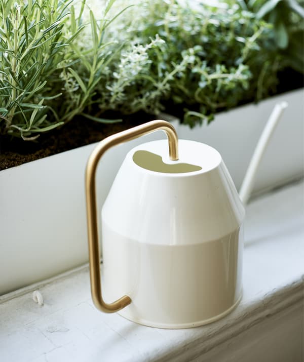 Close-up of a cream and gold watering can on a windowsill.