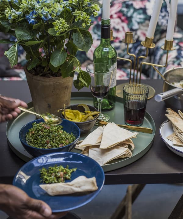 Close up of a dining table with a green tray with bowls of food and a pair of hands dishing food onto a plate.