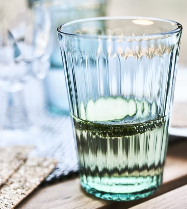 Close-up of a green glass filled with liquid and cucumber slices.