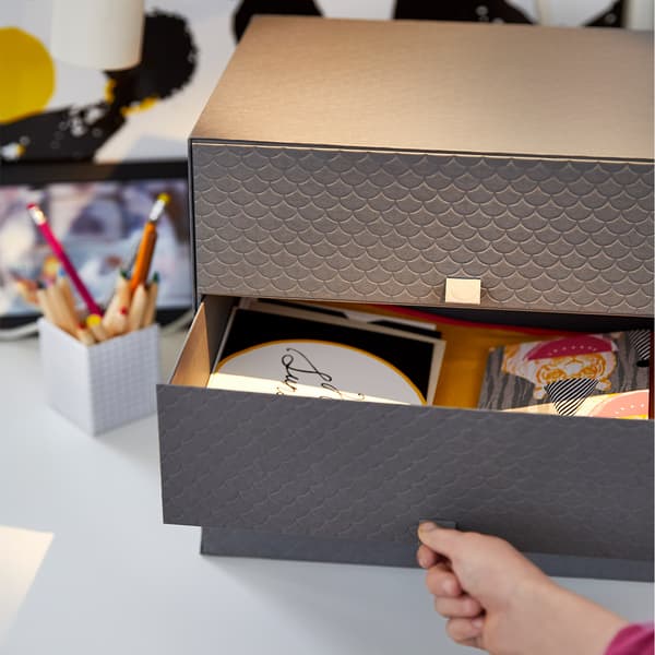 Close-up of a grey paper mini chest with three drawers, one of them is open.