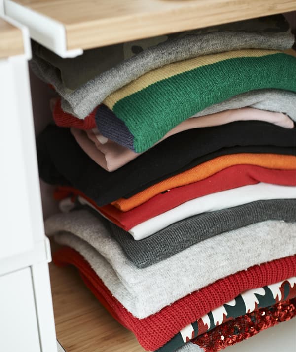 Close up of a pile of colourful folded knitwear on a shelf.