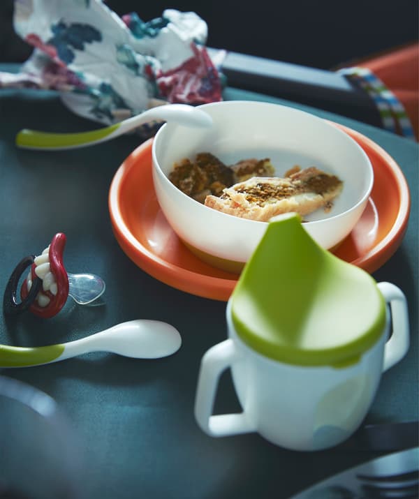 Close-up of a tableware suitable for a small child, including a drinking beaker, child friendly feeding spoons and a bowl.