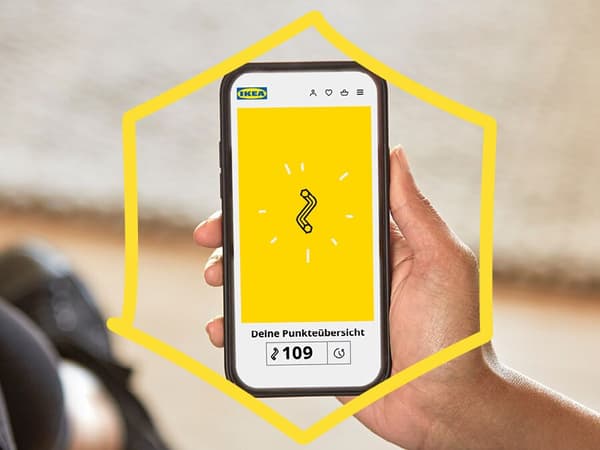 Close up of a woman looking at her smartphone. The phone shows a yellow background with an Allen key symbol of the IKEA loyalty programme.