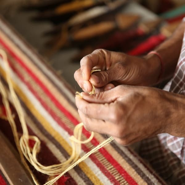Close-up of a woman weaving a rug by hand.