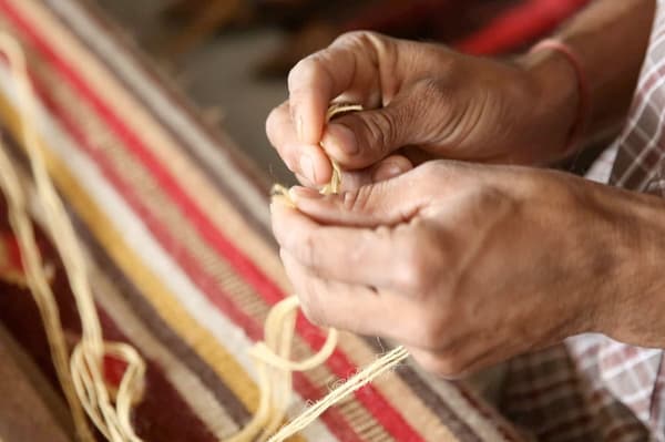 Close-up of a woman weaving a rug by hand.