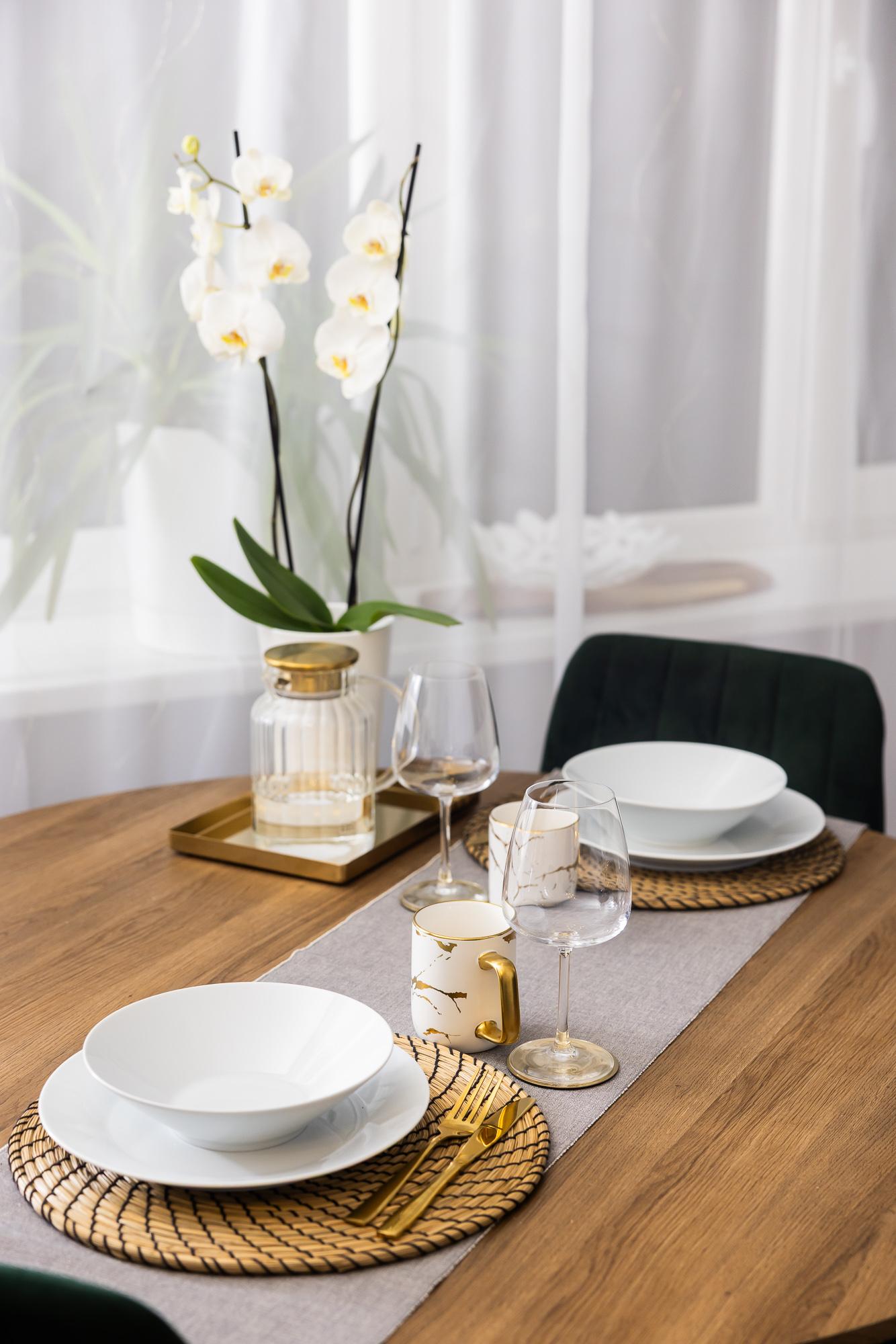 Close-up of a wooden table set with white plates, glassware and a white orchid arranged on a decorative tray.