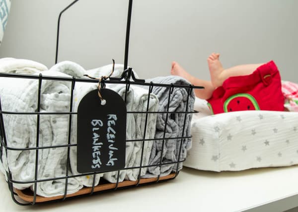 Close up of black PLEJA wire caddy, filled with receiving blankets, with a baby's kicking feet in the background.