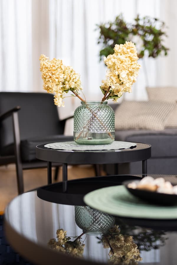 Close-up of decorative vase with dried flowers on black coffee table in living room.