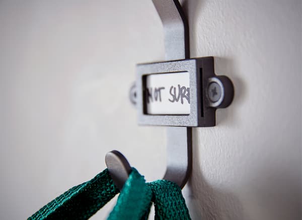 Close-up of green bag handles hung over a black hook with a hand-written name tag.