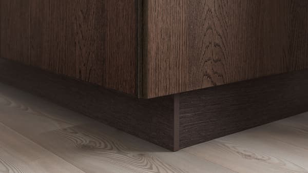 Close-up of the corner of a kitchen cabinet where it meets the floor, which is a gray wood floor.
