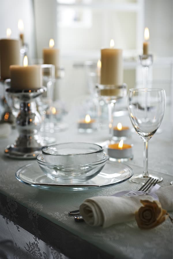  Close-up of warmly lit candles in glass candlesticks next to glass dinnerware.