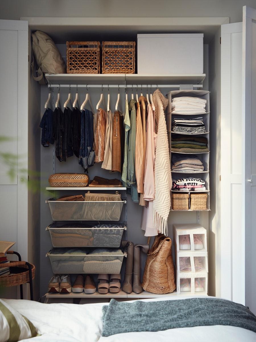 Clóset de ropa blanco BOAXEL alto. Está lleno de ropa colgada en ganchos y ordenado también con cajones plásticos y espacio para guardar zapatos.
