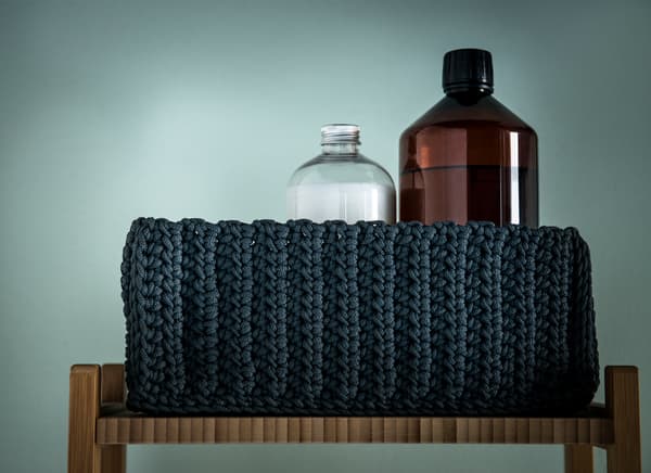 Closeup of a black woven fabric basket storing bathroom supplies.