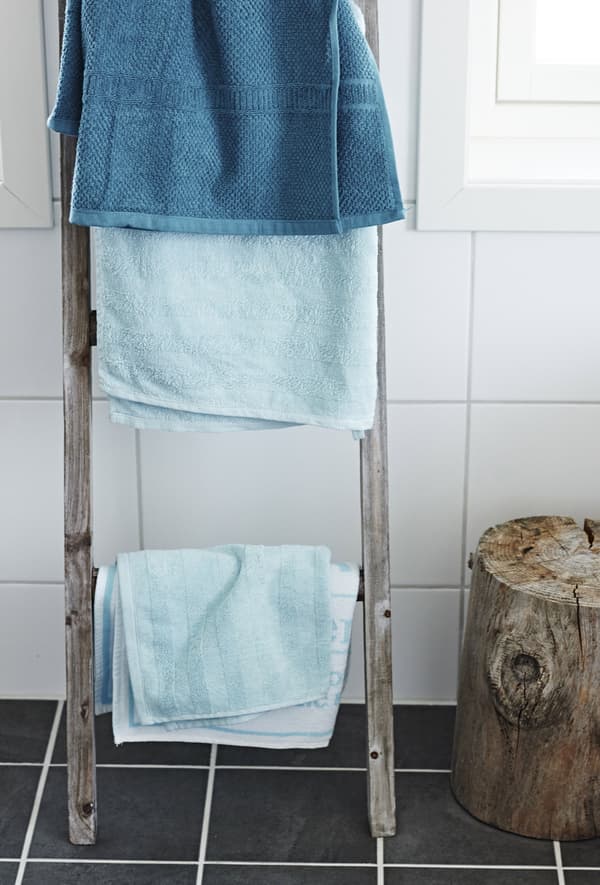 Closeup of a wood drying rack with bright blue hand towels and bath towels as an accent colour.