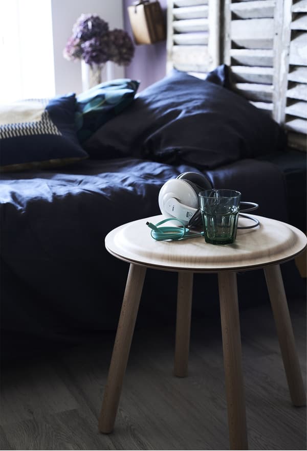 Closeup of a wooden stool being used as a bedside table to hold headphones and a glass of water.
