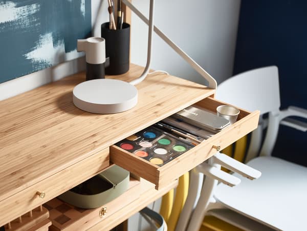 Closeup of an IKEA SVALNÄS shelving unit, with a slim drawer opened showing watercolour paints and art supplies inside.
