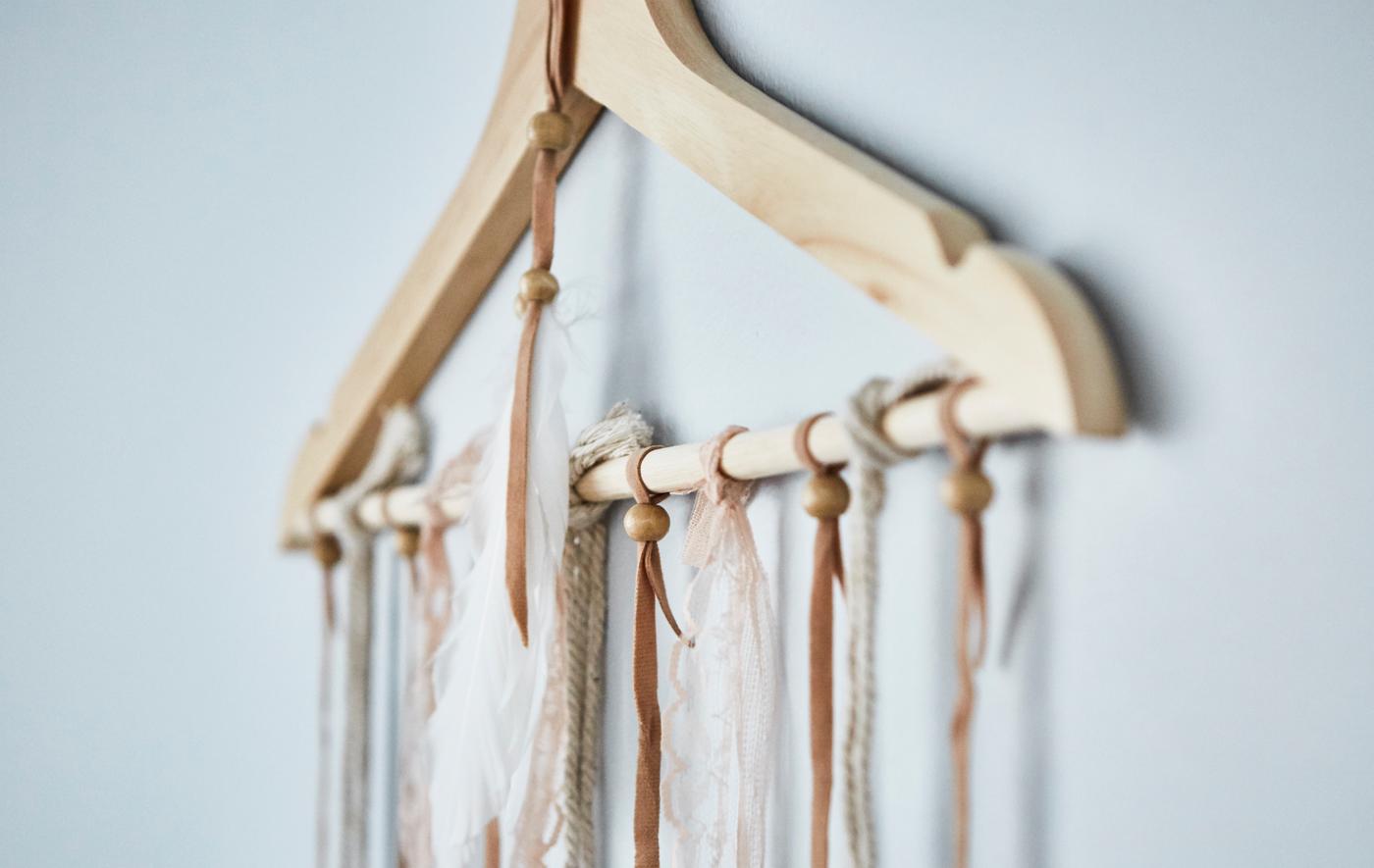 Closeup of fabric and beads hanging from an IKEA BUMERANG wooden hanger on a blue wall.