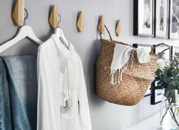 Clothes and a basket hanging on wooden hooks on a grey wall.