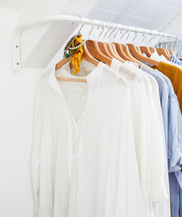Clothes hanging on wooden hangers on a white rail in a white room.