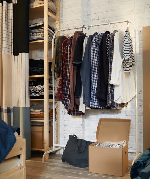 Clothing hung on the MULIG clothing rack in a closet space with open shelving against a white brick wall.