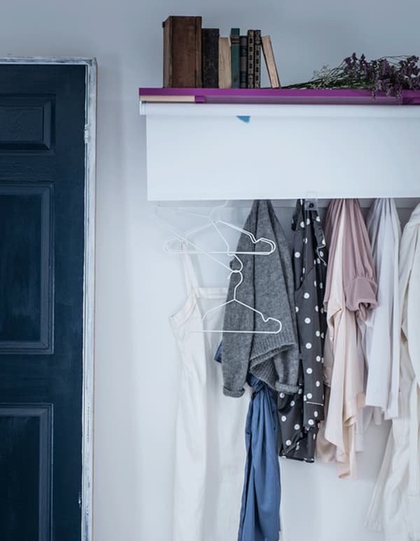 Clothing hung on wall hooks under a shelf and hidden by a hand-painted TUPPLUR blackout blind.