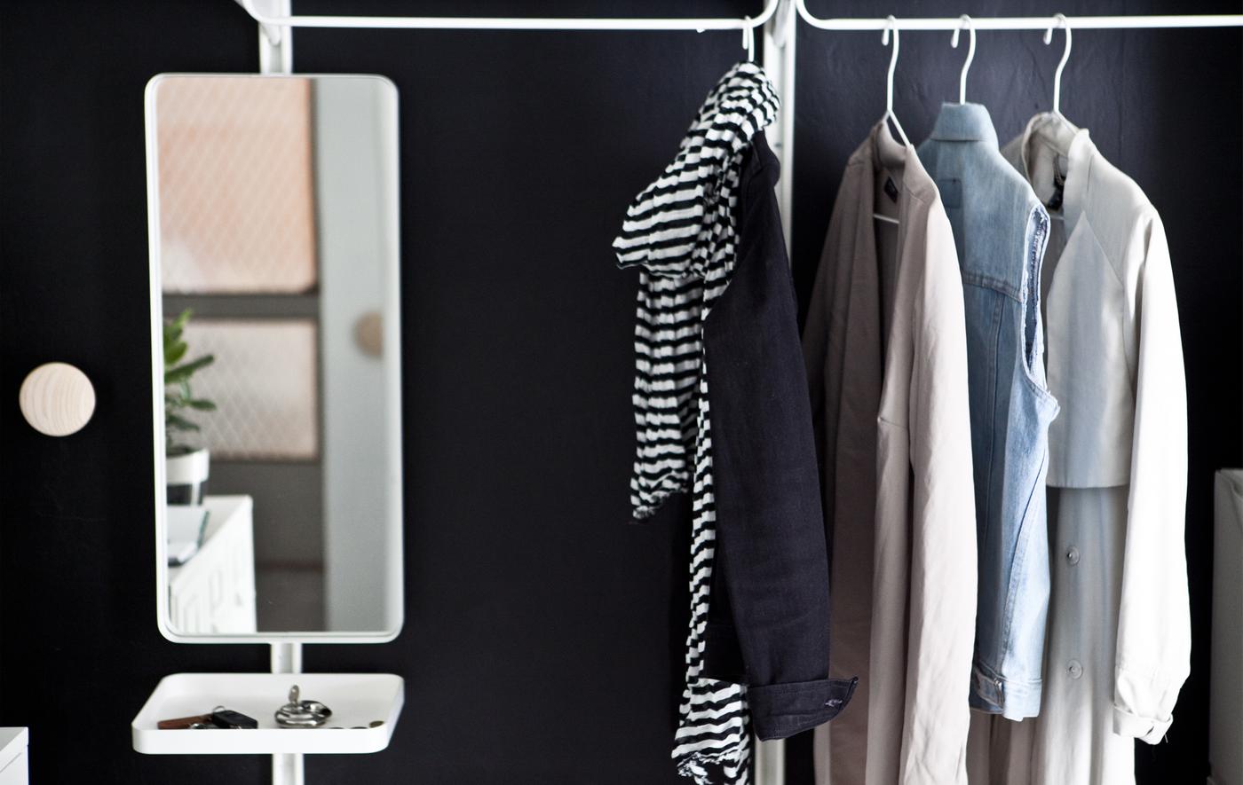 Coats, jackets and a mirror with a small tray hanging on a rail against a black wall.