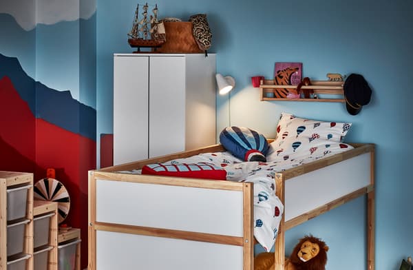 Coin d’une chambre d’enfant occupé par un lit réversible en position mezzanine, étagère murale avec livre et jouets, et applique allumée.