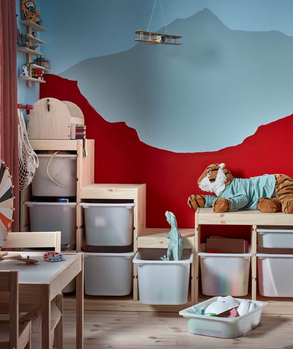 Coin d’une chambre d’enfant où la ligne inégale formée par une étagère remplie de jouets se fond dans les couleurs du mur à l’arrière-plan.