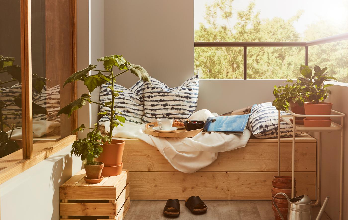 Coin sur le balcon avec un plan surélevé en bois, sur lequel se trouvent des coussins, du linge de lit et un plateau avec un déjeuner.