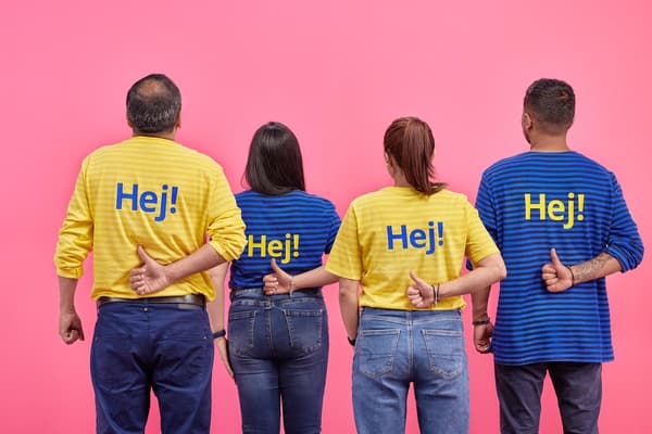 Colaboradores de IKEA usando sus poleras azules y amarillas levantando el dedo positivo en sus espaldas.