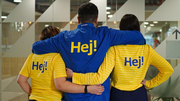 Colaboradores o trabajadores de IKEA compartiendo dentro de la tienda. Hay hombre y mujeres, vestidos con sus uniformes azules y amarillos, los colores de la bandera de Suecia. Foto de espalda.