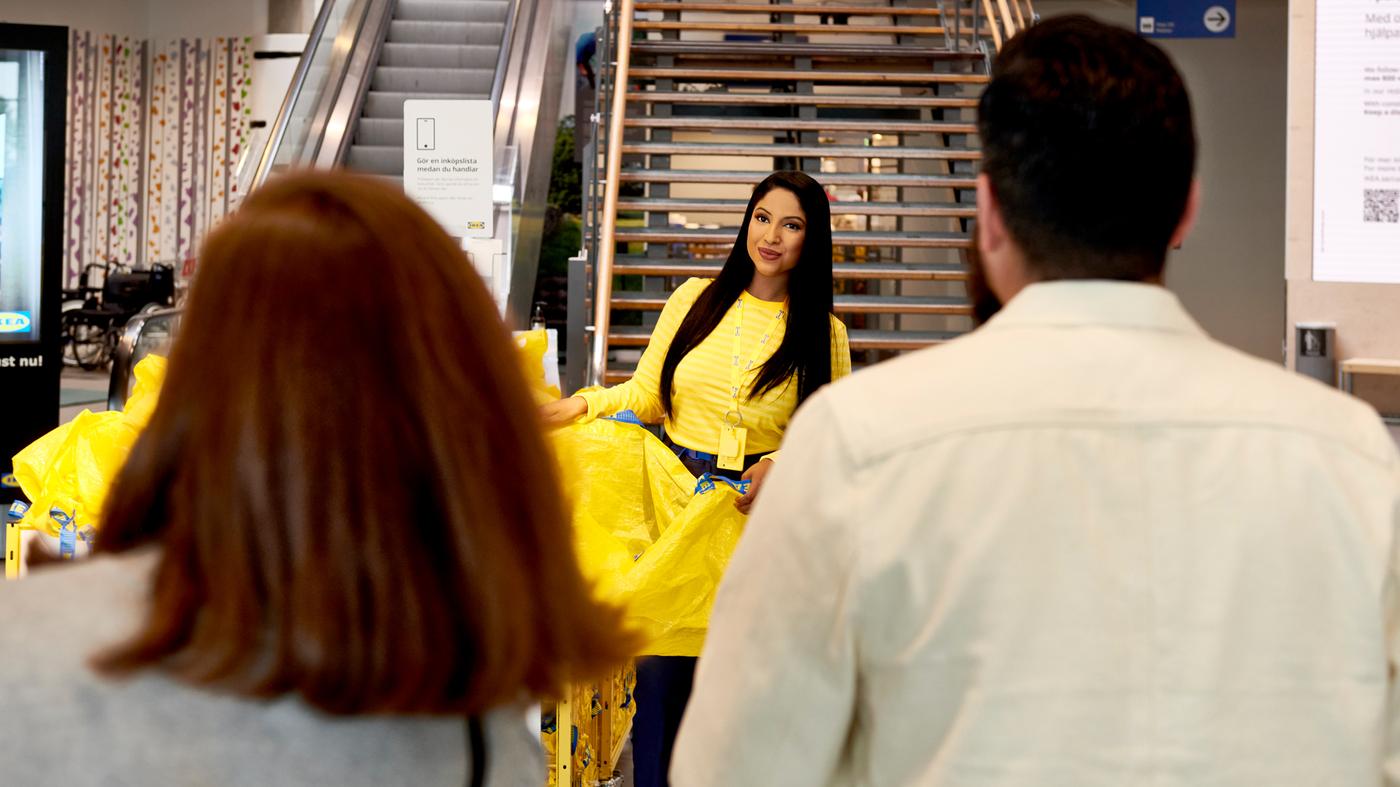 Collaboratrice IKEA en uniforme portant un sac jaune et descendant les escaliers d’un magasin IKEA pour accueillir des clients.