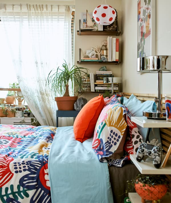 Colorful textiles on a bed with storage on the headboard and wall shelves.