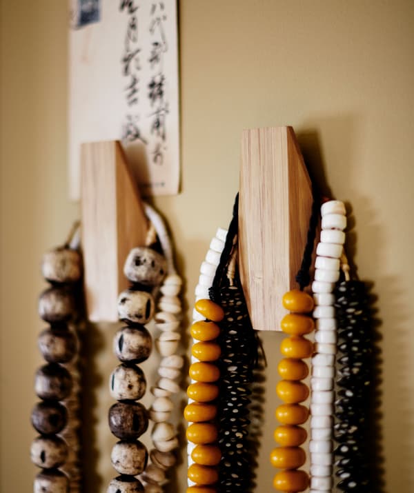 Colourful beaded necklaces hanging from two wooden hooks.